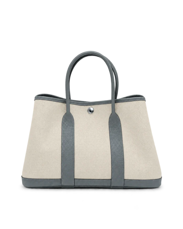 Upright front view of a cream canvas tote with grey-blue leather handles and trim and a silver snap