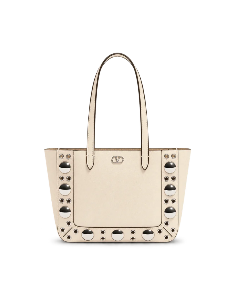Upright front view of a cream long-handle tote with silver dome studs and circular eyelets