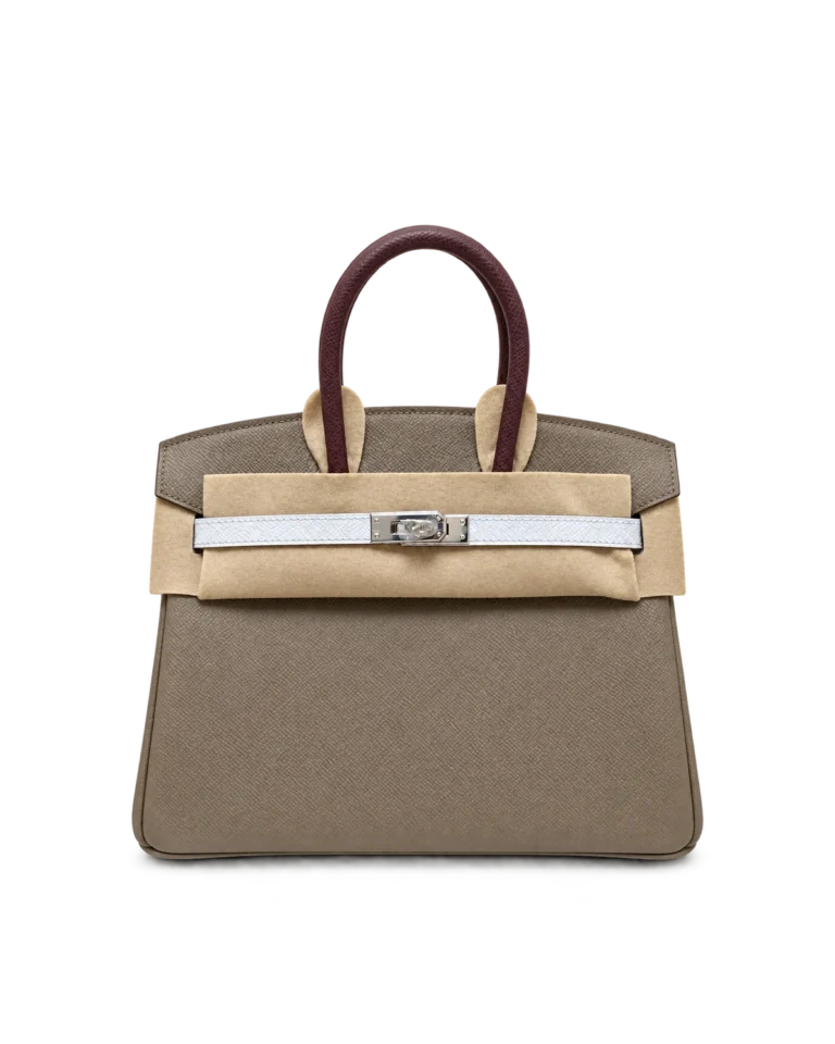 Upright front view of a taupe textured top-handle bag with a burgundy handle, white closure strap and protective felt