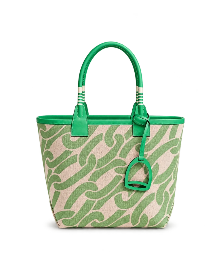 Upright front view of a green patterned canvas tote with green leather handles and a stirrup-shaped charm